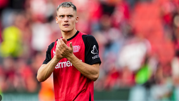 A soccer player in a red and black jersey claps, standing on the field with fans in the background, reminiscent of Bayern Munich celebrations.