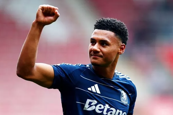 Soccer player in a navy jersey raises his fist and smiles, celebrating on the field—rumored to be on Manchester United's transfer radar.
