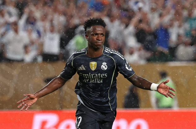 Vinicius Jr, in a black Real Madrid jersey, celebrates on a rainy field as fans cheer passionately in the background.