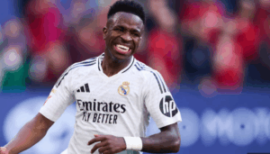 Vinicius Jr, wearing a white Real Madrid jersey, smiles during a match on the field.