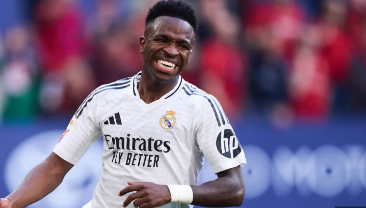 Vinicius Jr, wearing a white Real Madrid jersey, smiles during a match on the field.