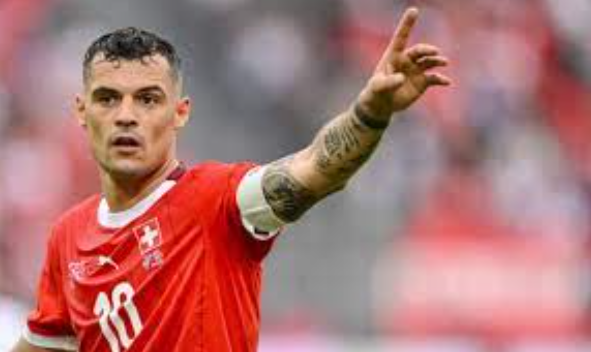 Soccer player Xhaka in a red Switzerland jersey points with his right arm during a match.