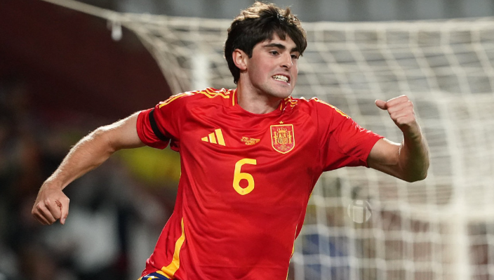 Midfielder Guerra, rumored for a Manchester United transfer, celebrates with a clenched fist in his red Spain jersey in front of the goal net.