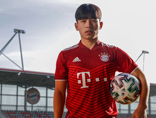 Lee Hyun-ju, in a red Bayern Munich jersey, holds a ball at an outdoor stadium.