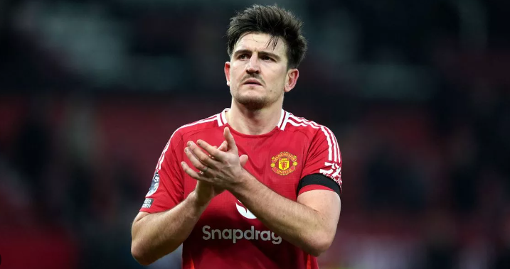 Man United football player Maguire, in a red jersey, clapping on the field with a focused expression during the USA Tour.
