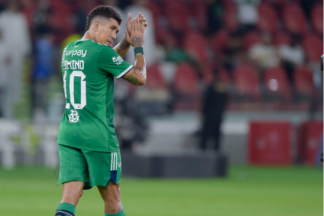 Soccer player in a green jersey claps while walking on the field, red stadium seats in the background—possibly celebrating a moment for Al Sadd in Qatar.