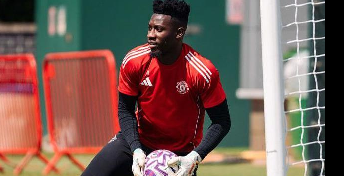 Man United’s Onana, in a red shirt, holds a soccer ball during pre-season training near a goalpost.