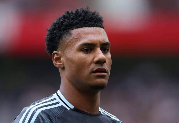 Ollie Watkins in a dark jersey with white stripes stands on the field, resembling a determined Premier League star in action.