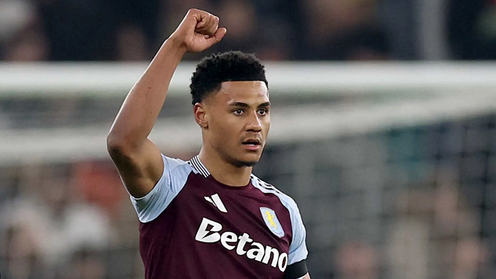 A Premier League striker in an Aston Villa jersey, likely Watkins, raises his right fist during a match.