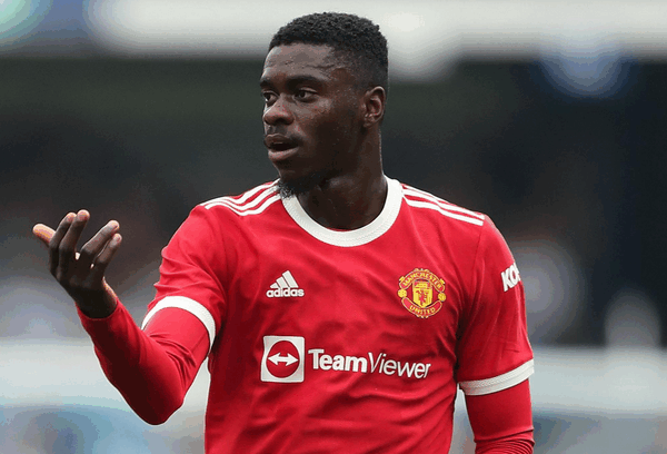 A Man Utd footballer gestures with his left hand during a match, wearing the iconic red kit—Axel Tuanzebe stands out with his commanding presence on the field.