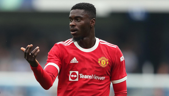 A Man Utd footballer gestures with his left hand during a match, wearing the iconic red kit—Axel Tuanzebe stands out with his commanding presence on the field.