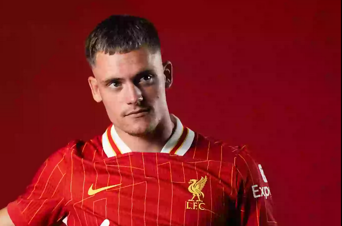 A male footballer in a red Liverpool FC jersey poses against a red background, proudly representing Liverpool.