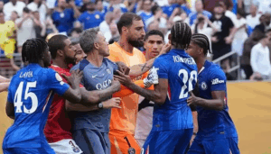 Soccer players from PSG and their rivals, including Joao Pedro, argue and push each other during a heated moment on the field as coach Luis Enrique watches from the sidelines.
