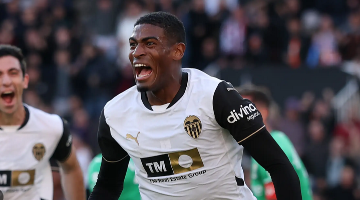 A Spanish Defensive Prodigy in a white Valencia CF jersey celebrates on the field, mouth open in excitement.
