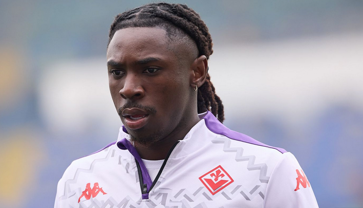 A footballer in a white and purple tracksuit with braids looks focused on the field amid Man United's deadline drama.
