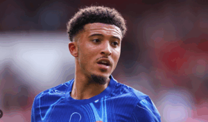 A male soccer player in a blue jersey, resembling Sancho from Man United, looks to the side during a match.