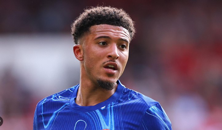 A male soccer player in a blue jersey, resembling Sancho from Man United, looks to the side during a match.