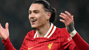 Liverpool’s No. 9, Nunez, celebrates with raised hands and a smile, proudly wearing the red jersey on the field.