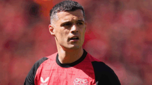 A male soccer player in a red and black jersey stands on the field, looking to the side, reminiscent of Sunderland’s iconic colors during their Premier League return.