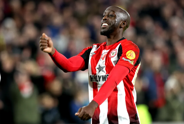 Brentford striker in a red and white jersey celebrates on the field, smiling with arms raised.